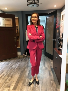 Maura in a fuchsia pantsuit in a "boss" pose with her arms crossed.