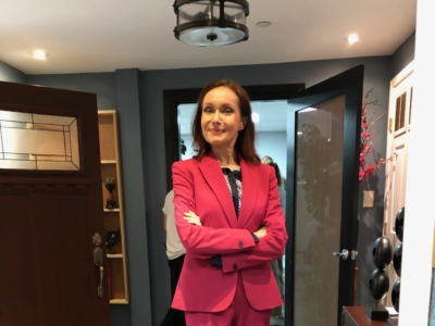 Maura in a fuchsia pantsuit in a "boss" pose with her arms crossed.